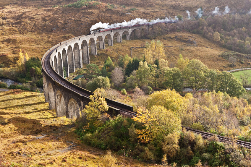 The steam locomotive 'The Jacobite' hauling its maroon livery coaches across Glenfinnan Viaduct on an autumn day in the Scottish Highlands. Always a noted attraction for railway enthusiasts the world over, it recently gained wider fame as a location venue for the Harry Potter films with the 'Hogwarts Express'.